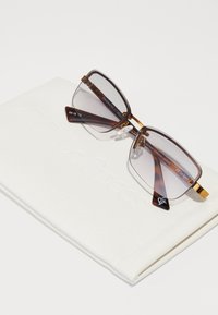 Ochelari de soare dreptunghiulari, cu model broască țestoasă maro, lentile cu gradient gri, accente aurii și punte nazală transparentă, odihnindu-se pe un etui alb.