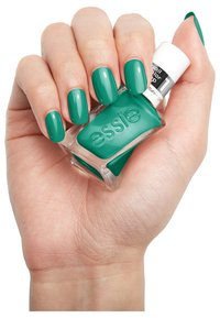 Groene nagellak in een doorzichtige glazen fles met een witte dop. Hand toont netjes gelakte nagels met een glanzende afwerking.