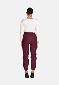Witte langemouwen top en bordeauxrode joggingbroek met elastische taille en taps toelopende boorden, gedragen met zwarte hoge hakken. Achteraanzicht.