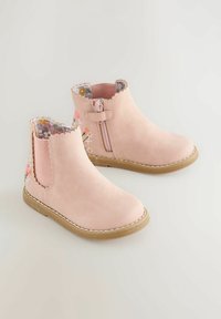 Botines de ante rosas con forro de estampado floral, bordes ondulados, cremallera lateral y suela de goma texturizada.