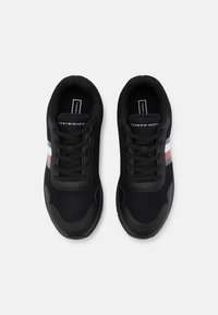 Baskets noires Tommy Hilfiger avec lacets, avec des bandes blanches, rouges et bleues sur les côtés et le nom de la marque sur la languette, vues de dessus.