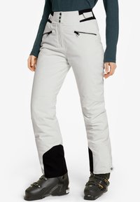 Pantalones de nieve blancos con un diseño de cintura alta, con acentos negros, bolsillos con cremallera y una textura suave, combinados con botas de esquí negras.
