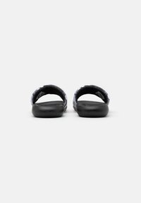 Sorte svarte sandaler med teksturerte stoffstropper, åpen bak, og myk polstret fotbed. Sklisikker såle med minimalistisk design.