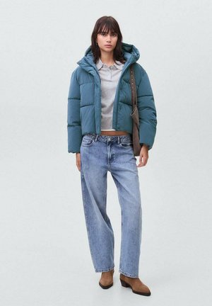 Türkisfarbene kurze Pufferjacke mit Kapuze, darunter ein graues Poloshirt, hellblaue weit geschnittene Jeans und braune hochhackige Ankle Boots. Einfaches Design.