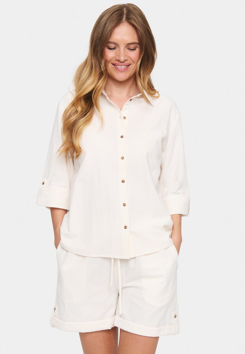 White, button-up shirt with a collar and three-quarter sleeves, paired with white shorts featuring folded cuffs and drawstring waist.