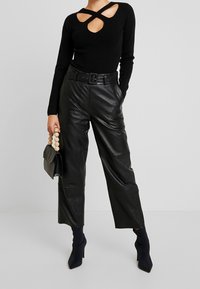 Svart stickad topp med utskärningsdesign, kombinerad med högmidjade svarta läderbyxor. Kompletteras med en svart clutch och en beige pärlhank.