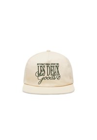 Casquette beige à visière plate, ornée d'un texte brodé vert "INTERNATIONAL SPORTING LES DEUX GOODS." Le tissu est lisse avec un léger éclat.