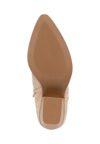 Zapato de tacón alto beige con punta afilada y suela texturizada. Presenta acentos decorativos y un material superior suave similar al ante.