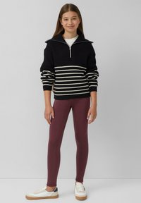 Zwart gebreid sweater met witte strepen, ritssluiting aan de kraag, gecombineerd met kastanjebruine leggings en witte sneakers met tan accenten.