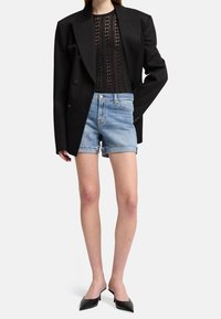Czarna, dwurzędowa marynarka na prześwitującej, czarnej bluzce w wzory, zestawiona z jasnoniebieskimi szortami dżinsowymi z postrzępionymi brzegami oraz czarnymi butami z zaostrzonym noskiem.