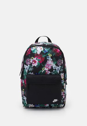 Černý batoh s vícerozměrným květinovým vzorem, přední kapsou na zip, horním madlem a bílým logem Nike na kapse.