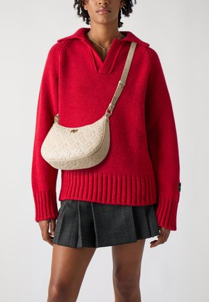Pull en maille rouge avec un col en V et un ourlet côtelé, associé à un sac en cuir beige avec un logo embossé et une bandoulière plate.