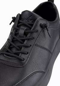 Baskets en cuir noir avec une surface texturée, un design traditionnel à lacets, et une ligne de couture accentuée sur le côté.