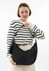 Bolso tejido negro con forma curvada y acentos de cuero. Presenta un borlón desmontable, un asa y una textura estructurada.