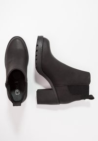 Botines negros, hechos de material suave, con puntera redondeada, paneles laterales elásticos y un tacón grueso con suela texturizada.