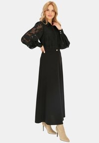 Czarna, półprzezroczysta bluzka z długim rękawem w kwiatowy wzór, zestawiona z długą czarną spódnicą i beżowymi botkami na obcasie; detal w postaci guzika w talii.