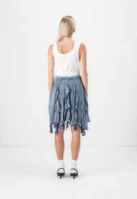 Lichtblauwe denim rok met ruffles, met een gelaagd ontwerp. Gecombineerd met een witte geribde tanktop en zwarte schoenen met enkelsokken.
