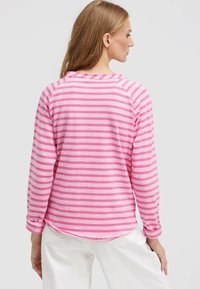 Langärmliges Oberteil in Pink und Weiß mit Streifen, runder Halsauschnitt und leichtem High-Low-Saum; einfarbige pinke Bündchen und lässige Passform.