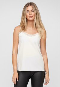 Ivory camisole top met kantafwerking langs de halslijn. Gemaakt van soepel materiaal, met dunne spaghetti banden en een relaxte pasvorm.