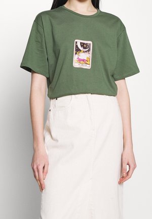 Oliwkowozielona bawełniana koszulka z krótkim rękawem, ozdobiona dekoracyjną grafiką karty tarota z motywem księżyca na środku. Połączona z kremową spódnicą.