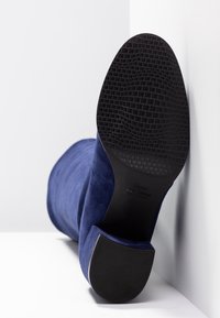 Navyblaue Wildleder-Ankle-Boots mit abgerundeter Spitze, niedrigem Absatz und strukturiertem schwarzen Gummisohle mit einem Logo-Muster.