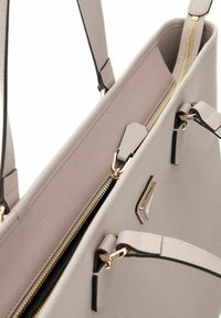 Borsa a mano sintetica beige con superficie texturizzata, zip dorata e dettagli neri. Caratterizzata da manici doppi e un dettaglio del logo sulla parte anteriore.