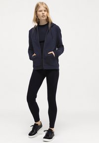 Marinblå zip-up hoodie med dragsko, två framfickor. Matchas med åtsittande marinblå leggings och svarta sneakers med vita sulor och snörning.