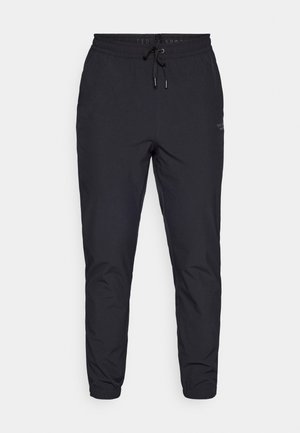 Melnās sporta bikses, kas izgatavotas no viegla materiāla, ar aukliņu jostasvieta, šauriem kājām un mazu logo detaļu sānos.