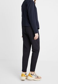 Veste bleu marine à coupe structurée, associée à un pantalon rayé noir et blanc. Baskets sportives de couleur claire avec des accents colorés.