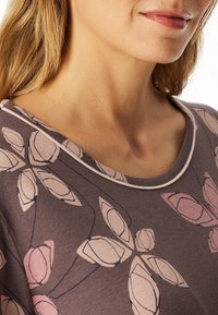 Brown top featuring a floral pattern in light pink and cream, with a scoop neckline and contrasting trim. Soft fabric texture evident.