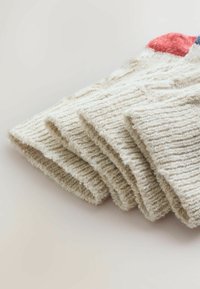 Złożone starannie beżowe skarpetki szydełkowane, z teksturowaną powierzchnią, z kolorowym akcentem na mankiecie w kolorze czerwonym, niebieskim i białym.