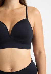 Bralette negro con escote profundo, tirantes delgados ajustables y material suave y elástico. Diseño sin costuras y sin hardware visible.