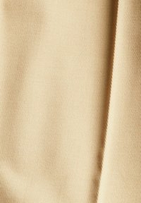 Gros plan d'un tissu côtelé beige avec un pli visible projetant une ombre sur le côté droit.