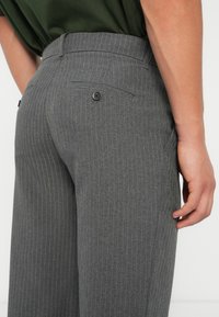 Gray pinstriped trousers featuring a flat front, a back pocket with a button, and a smooth texture. Adjusted waist for a fitted look.