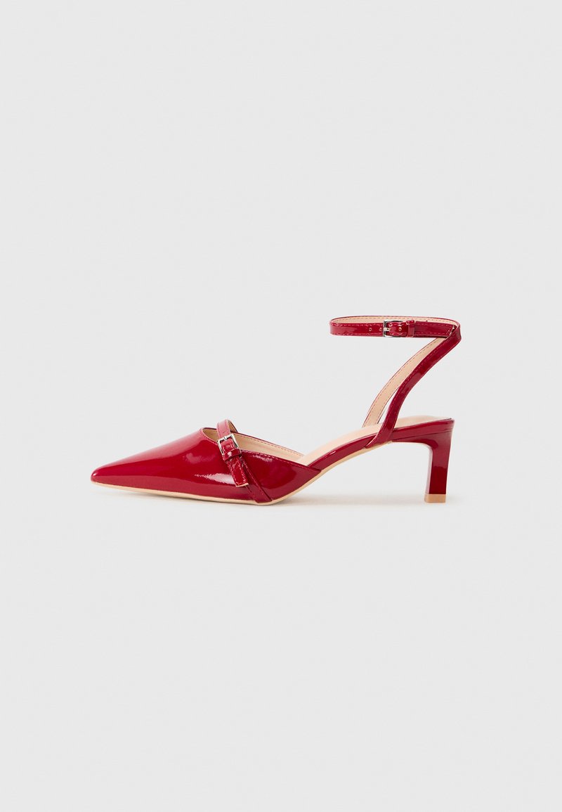Red patent leather heel with a pointed toe, ankle strap, and a low block heel. Features a decorative buckle detail.