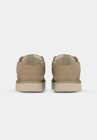 Beige sneakers med overdel i semsket skinn og mesh, med polstret krage og en strukturert, lysfarget gummisåle. Enkel design med minimale detaljer.