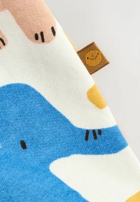 Baumwollstoff mit einem bunten abstrakten Muster, das rosa, blau, gelb und weiße Formen zeigt, einschließlich eines gestickten Etiketts mit einem Smiley-Gesicht.