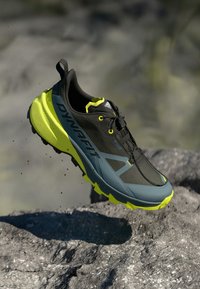 Παπούτσι trail running σε μαύρο και γκρι με νέον κίτρινες λεπτομέρειες, επάνω μέρος από διχτυωτό υλικό, ανθεκτική σόλα και δομημένο σύστημα κορδονιών για σταθερότητα.