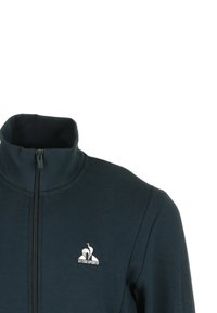 Chaqueta con cremallera en color azul marino, con un alto cuello, que presenta un logo blanco en el lado izquierdo. El material parece suave y texturizado, adecuado para un estilo de vestir casual.