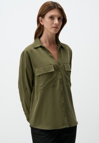 Olijfgroene, langekorte, knoopsluitende shirt gemaakt van zachte stof, met twee borstzakken en een relaxte pasvorm met kraagdetails.