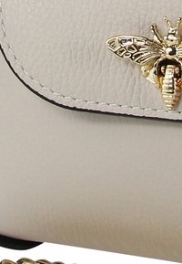 Lichtgrijze leren tas met een gestructureerde afwerking, voorzien van een gouden bijaccent op de klep en zwarte stiksels langs de randen.