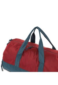 Bolsa de deporte roja y azul verdosa, fabricada con un tejido duradero, que presenta asas dobles, un cierre de cremallera en la parte superior y una superficie texturizada suave.