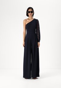 Navy jumpsuit with one shoulder and a lace long sleeve. Features wide legs and a fitted bodice, made of smooth, lightweight fabric.