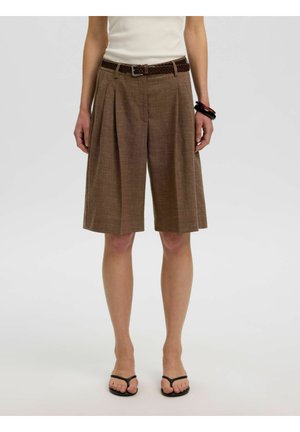 Braune plissierte knielange Shorts mit geflochtenem Gürtel, getragen mit schwarzen Sandalen, cremefarbenem Oberteil und Armbändern an einem Handgelenk.