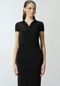 Crna polo haljina izrađena od glatkog, rastezljivog materijala. Ima dugmad sprijeda i kratke rukave, s uskim krojem i suknjom do poda.
