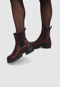 Bordeauxkleurige enkellaarzen met een zwart elastisch paneel met luipaardprint, een zijrits, een stevige zwarte zool en een trekkoord aan de achterkant.