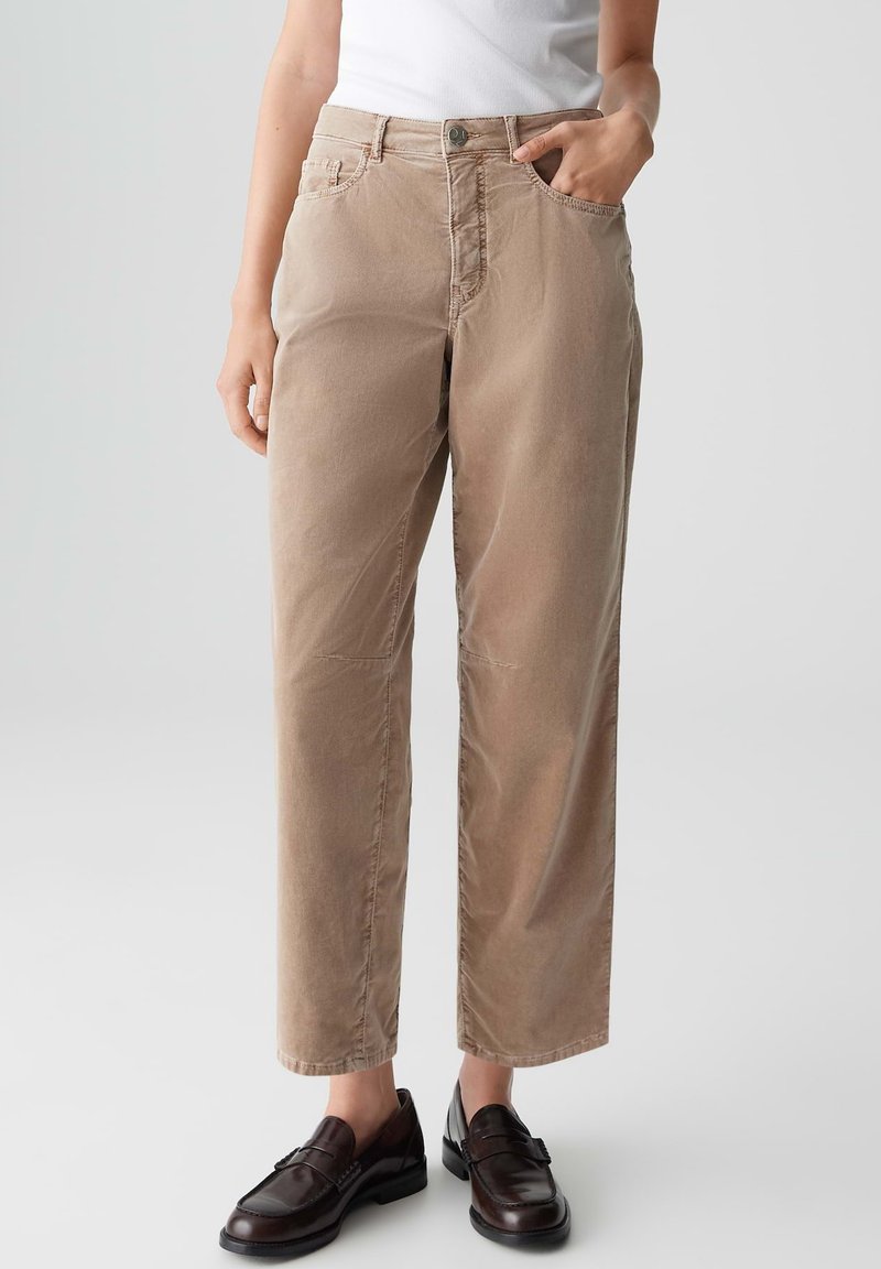 Pantaloni beige a gamba dritta con una superficie liscia, quattro tasche e chiusura a pulsante, abbinati a mocassini scuri.