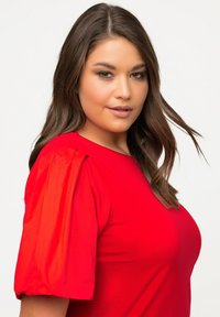Top rosso a maniche corte con maniche a sbuffo. Tessuto liscio, colore uniforme, design aderente e scollo a girocollo. Nessun motivo o dettaglio visibile.
