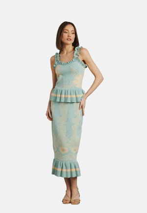 Helles blaues gestricktes Kleid mit Blatt- und Blumenmustern, ausgestelltem Saum, Rüschenträgern und einer taillierten Silhouette. Braune Sandalen mit Riemen.