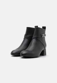 Botine negre din piele, cu vârf ascuțit, guler căptușit, detalii cu curea asimetrică și toc mic pătrat. Textură netedă.